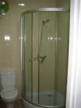 Ducha de esquina con mampara curva de cristal junto al inodoro del baño de la habitación
